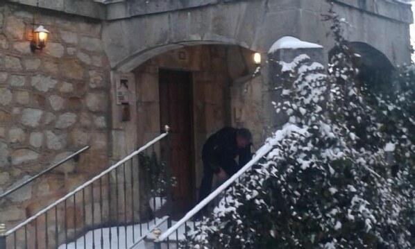 Un edificio de piedra con una puerta de madera, una barandilla metálica y árboles cubiertos de nieve.