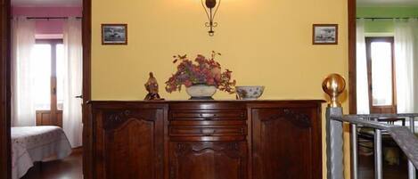 A room with a wooden dresser, a vase with flowers, and a wall-mounted light fixture.