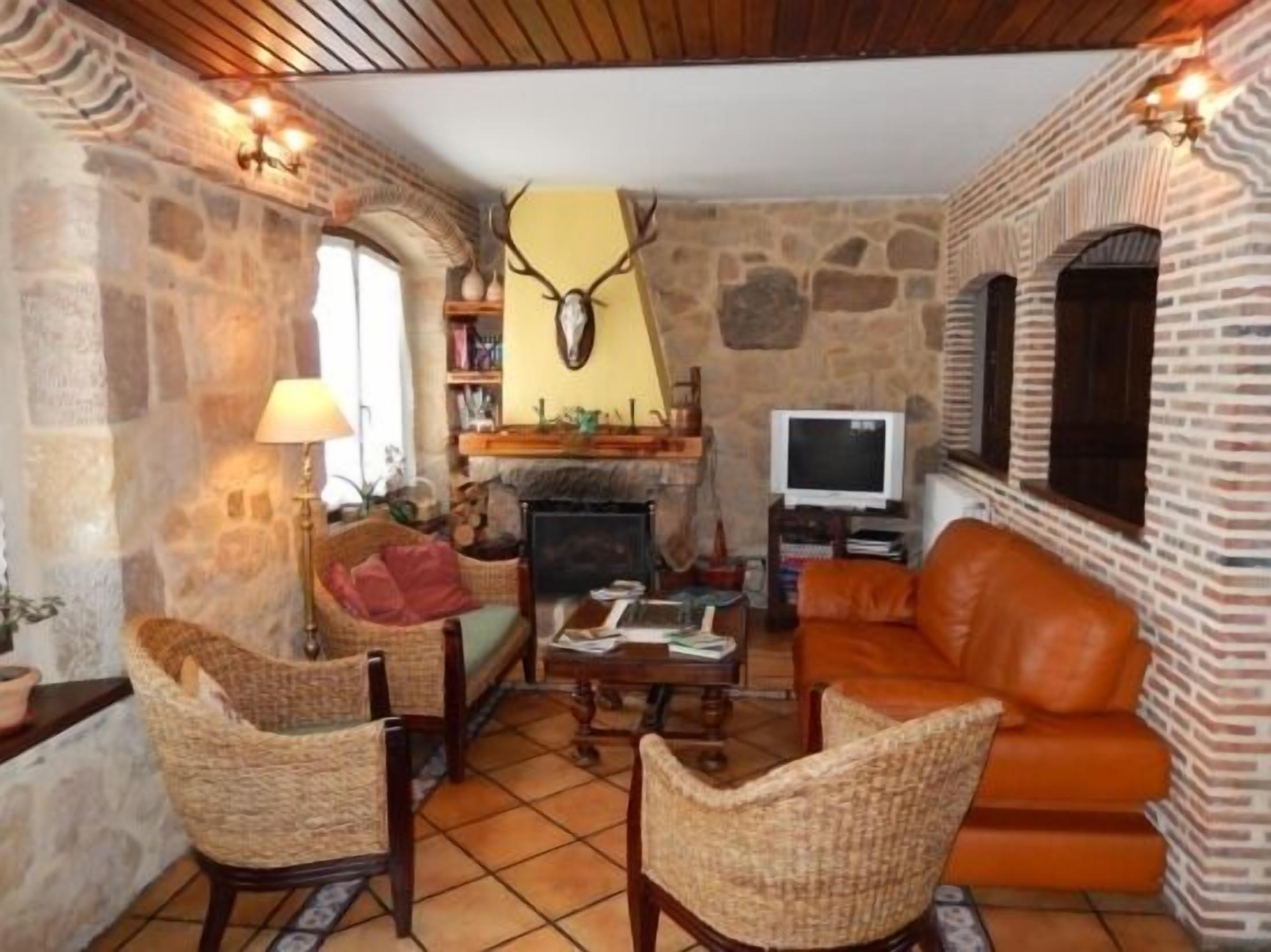 A cozy living room with stone walls, a fireplace, wicker furniture, and a television.