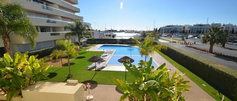 A modern hotel with a swimming pool, sun loungers, and palm trees.