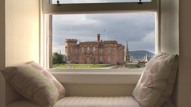 Asiento junto a la ventana con cojines, con vistas a un edificio histórico que tiene una torre y un puente al fondo.