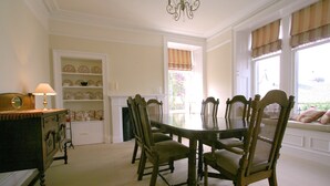Comedor con una mesa redonda y seis sillas, un aparador con una lámpara y un estante con objetos decorativos.