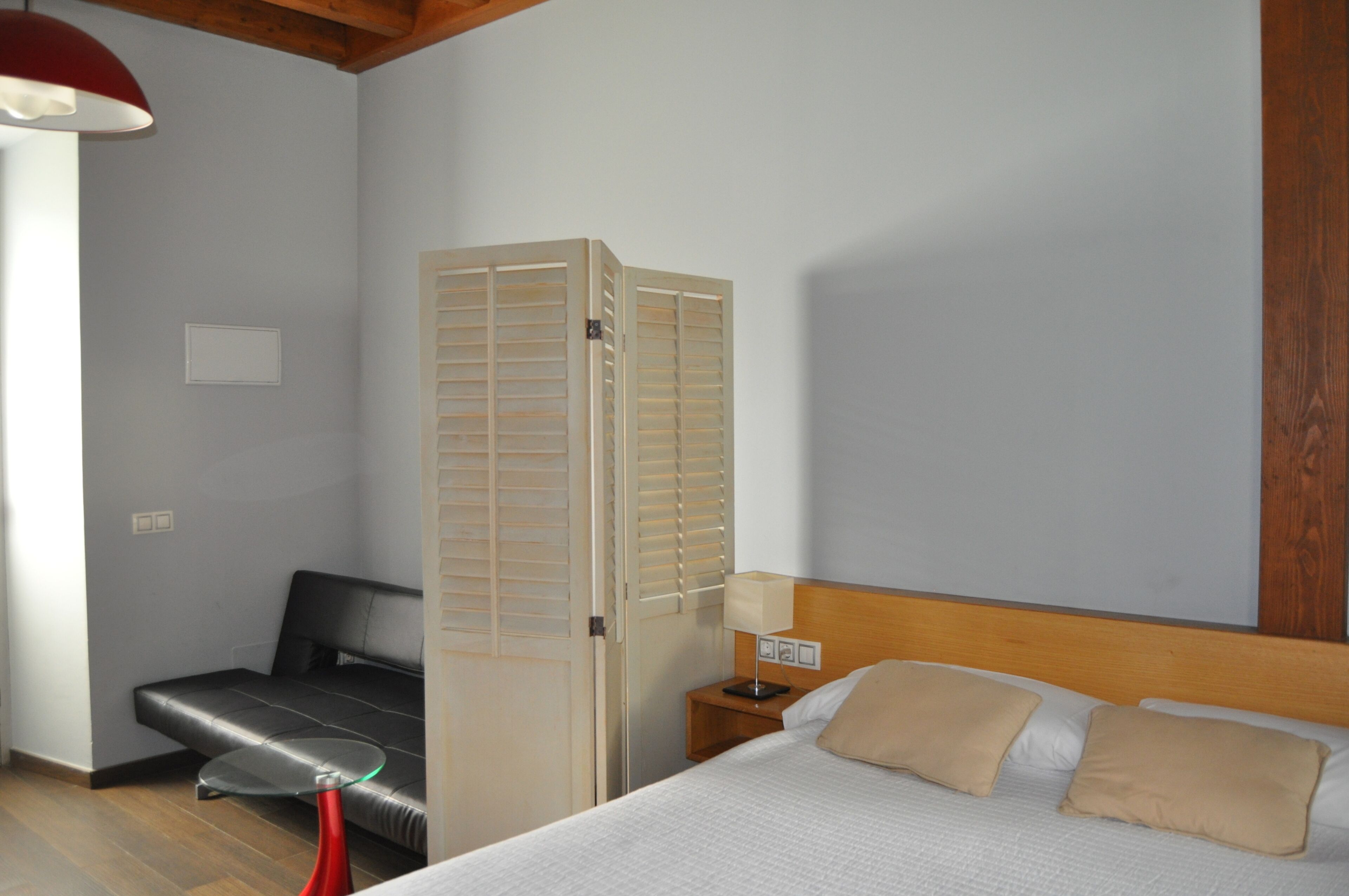 Una habitación de hotel con cama, mesita de noche, lámpara, una silla roja y un armario de madera.