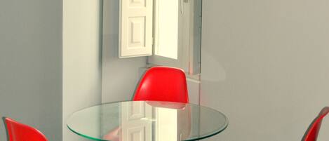 Une pièce avec une table en verre et des chaises rouges, une porte blanche et un interrupteur sur le mur.