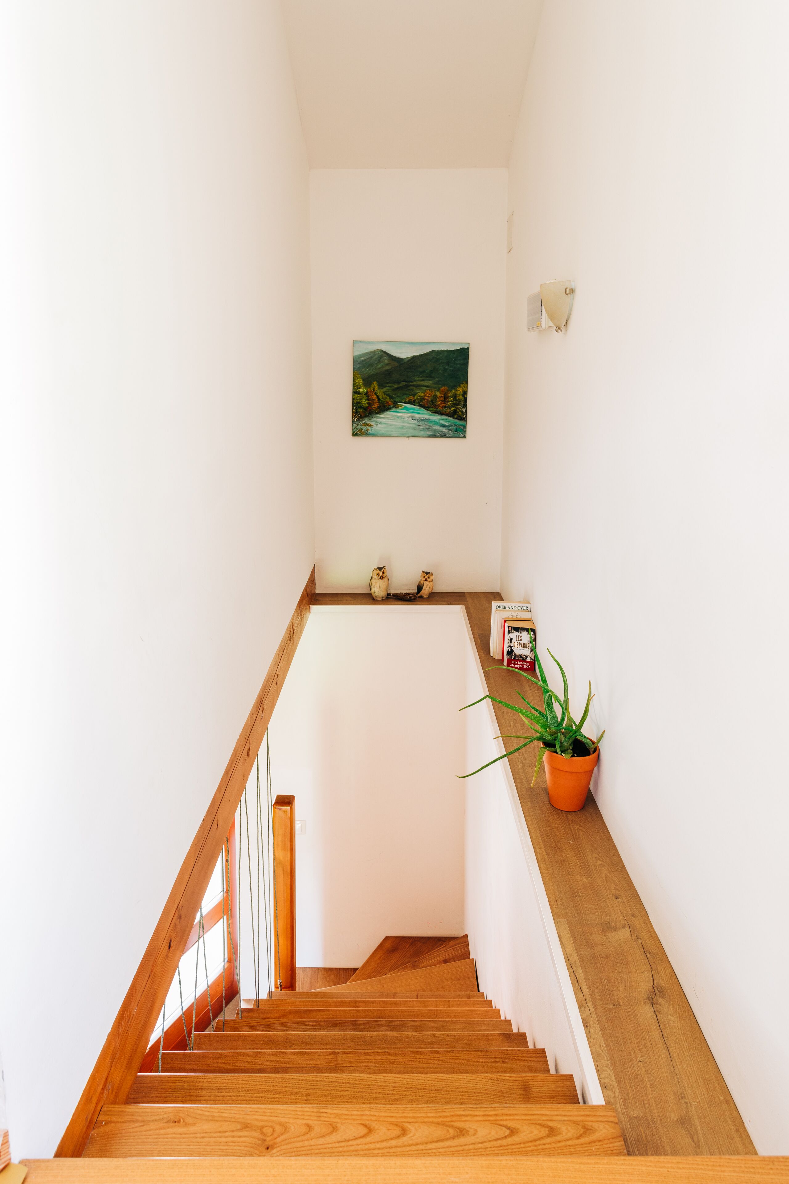 Una escalera de madera con paredes blancas y un cuadro de un paisaje.