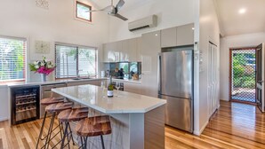 A modern kitchen with a central island, stainless steel appliances, and wooden bar stools. - Heliconia 10 Hamilton Island - oceanviews, buggy and transfers (Hamilton Island)