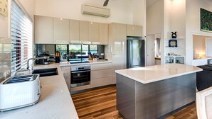 A modern kitchen with a large island, stainless steel appliances, and wooden flooring. - Heliconia 10 Hamilton Island - oceanviews, buggy and transfers (Hamilton Island)