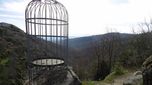 A metal birdcage on a rock with a view of a valley.