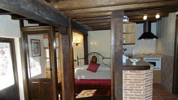 A bedroom with a bed, a wooden ceiling, a brick fireplace, and a window.
