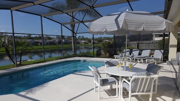 A poolside area with a covered seating area, a table, and chairs. - BrightwaterVilla. Lake view, west facing extra large pool deck, lanai, hot tub (Kissimmee)