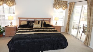 A bedroom with a large bed, two bedside tables, a nightstand, a lamp, a potted plant, and a sliding glass door leading to an outdoor area. - BrightwaterVilla. Lake view, west facing extra large pool deck, lanai, hot tub (Kissimmee)