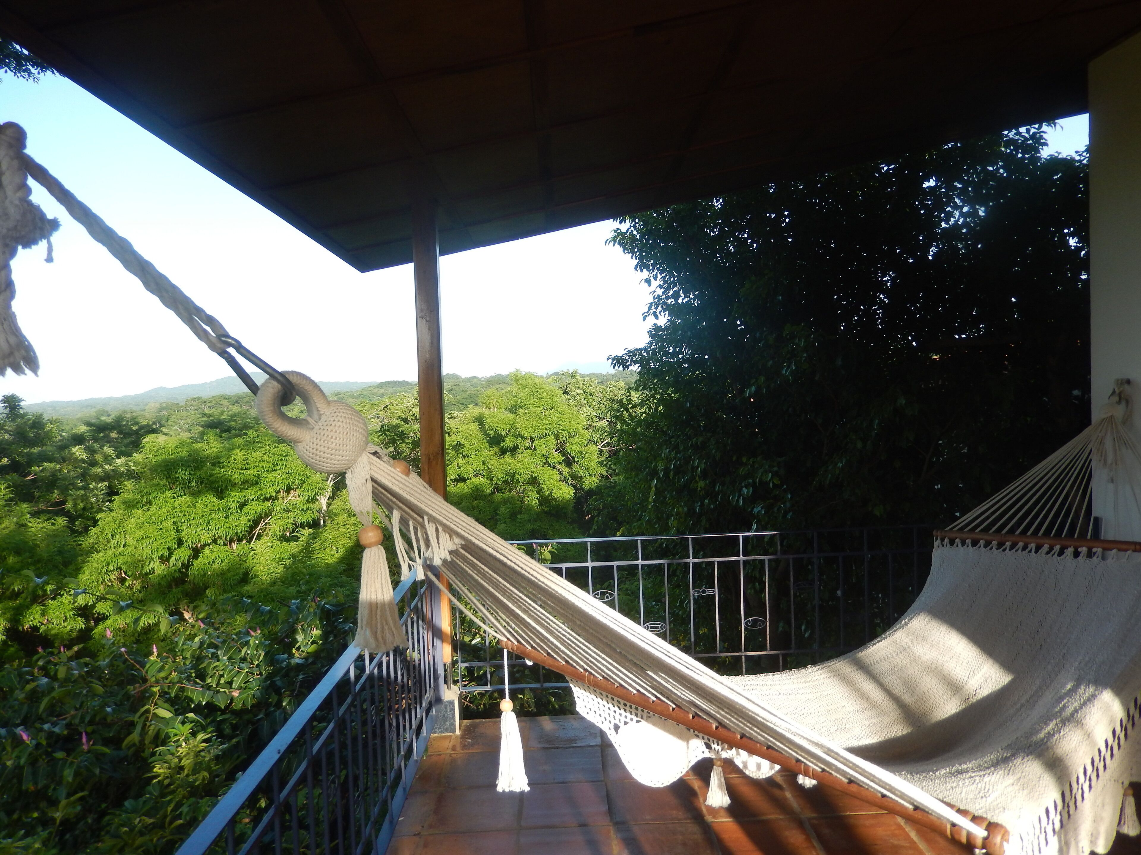 A hammock on a balcony with a view of a lush green landscape.