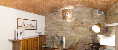 Un comedor con una mesa de vidrio, armarios de madera, paredes de piedra y un cuadro en la pared.
