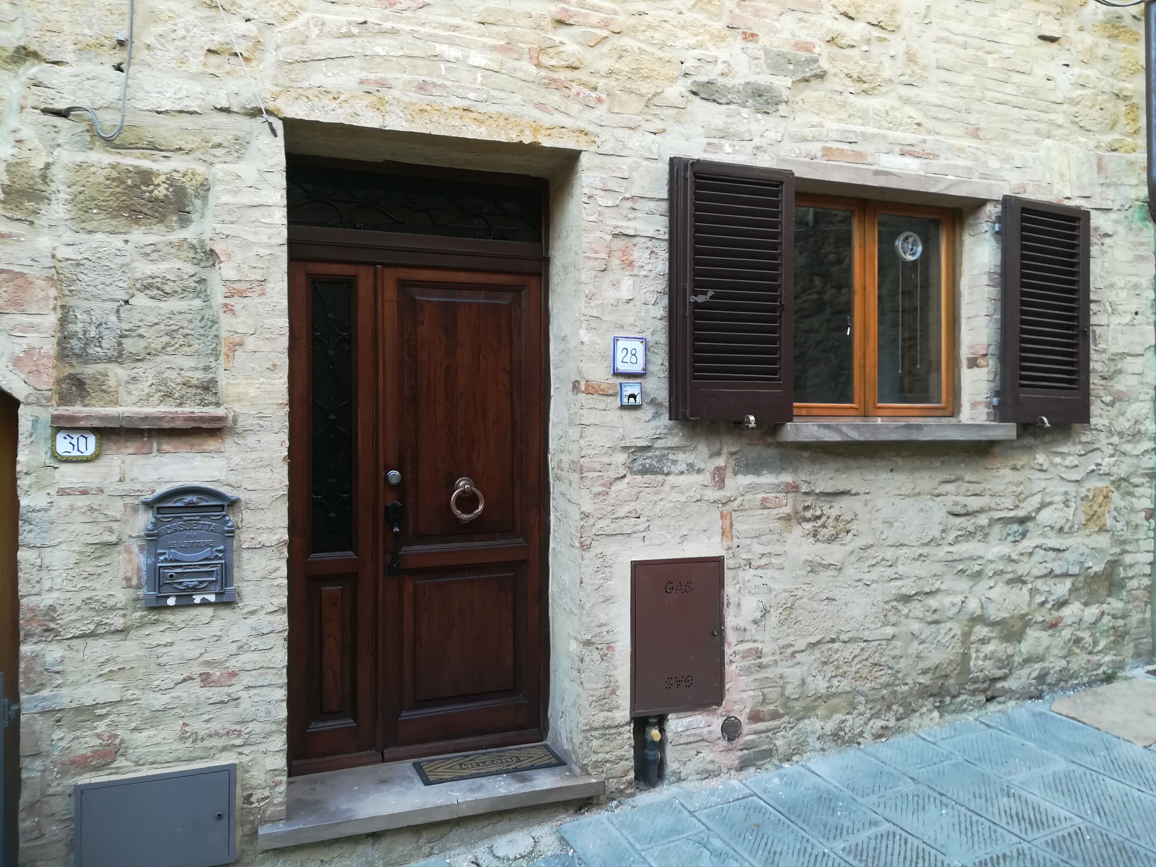 A stone building with a wooden double door, a window with shutters, and a small mailbox.