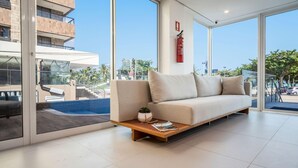 A modern living room with a sofa, a small table with a plant, and a view of a pool and building outside. - Hotel Praia Bonita Jangadeiros Pajuçara (Maceió)