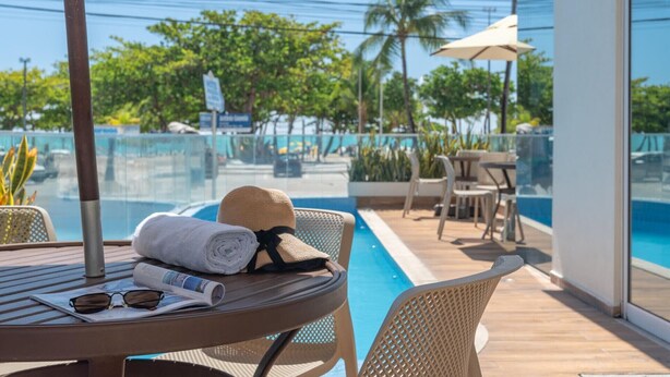 A poolside area with a table, a chair, a sun hat, and a towel. - Hotel Praia Bonita Jangadeiros Pajuçara (Maceió)