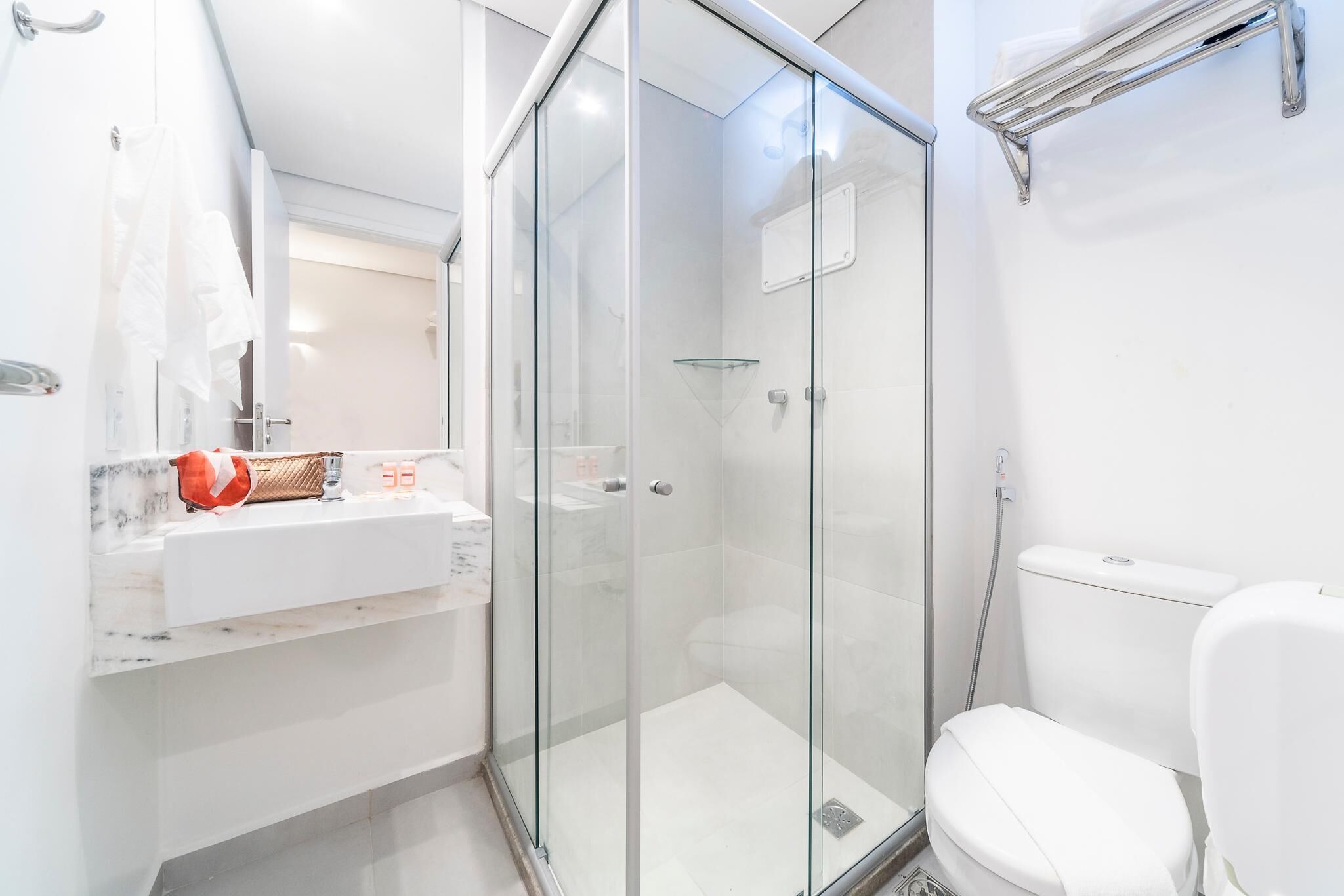 Un baño moderno con ducha de vidrio, un lavabo blanco con encimera de mármol y un inodoro blanco.