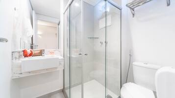 Un baño moderno con ducha de vidrio, un lavabo blanco con encimera de mármol y un inodoro blanco.