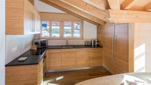 A modern kitchen with wooden cabinets, a black countertop, and a window providing natural light. - 5 Star Penthouse Apartment in Chalet Aberot !! (Wengen)