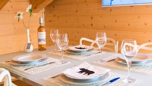 A dining table set with plates, glasses, and a bottle of wine, with a wooden wall and a TV in the background. - 5 Star Penthouse Apartment in Chalet Aberot !! (Wengen)