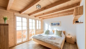 A wooden bedroom with a large bed, a nightstand, and a window with a view. - 5 Star Penthouse Apartment in Chalet Aberot !! (Wengen)
