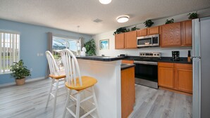 Une cuisine moderne avec des meubles en bois, des appareils électroménagers en acier inoxydable et un coin bar agrémenté de tabourets blancs.