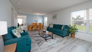 Un salon avec des canapés de couleur turquoise, une table basse en bois et un coin repas comprenant des chaises et une table en bois.