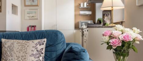 A modern living room with a blue sofa, a decorative pillow, and a vase of flowers on a wooden table.