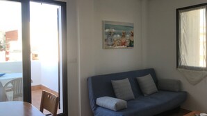 A living room with a blue sofa, a painting on the wall, and a window with curtains.