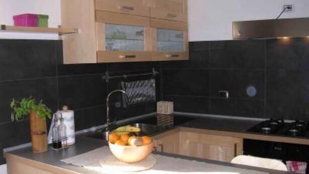 A modern kitchen with dark tiles, wooden cabinets, and a gas stove.