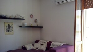 A living room with a purple sofa, a small table, and a wall-mounted shelf with decorative items.