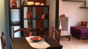 A dining area with a wooden table and chairs, a decorative mirror, and a bookshelf with various items.