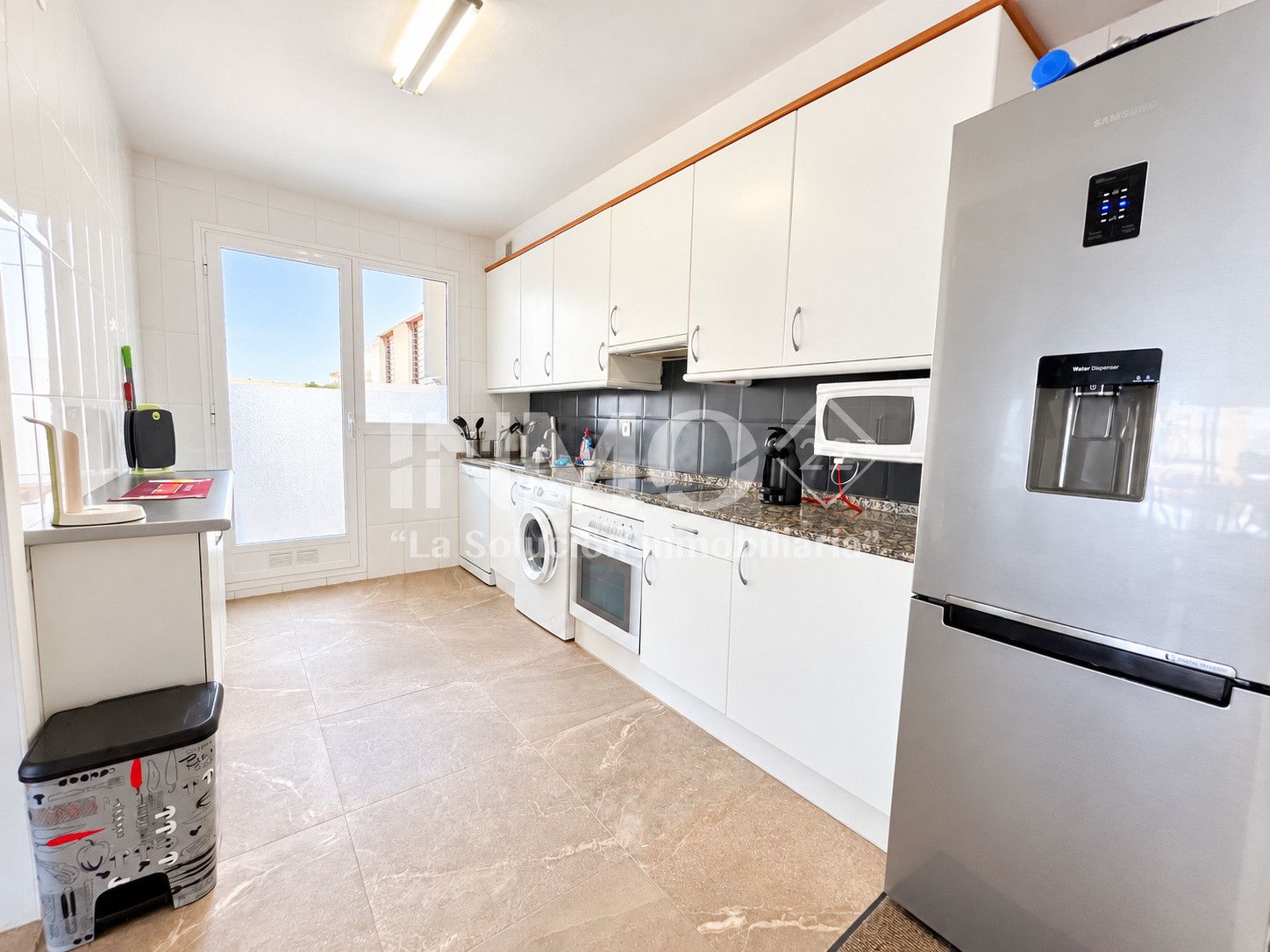 Een moderne keuken met witte kasten, een roestvrijstalen koelkast, een wasmachine en een magnetron.