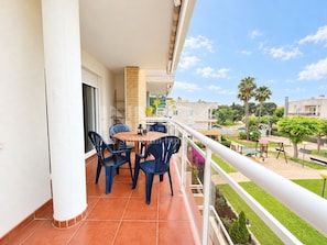 A balcony with a table and chairs, a railing, and a view of a residential area with greenery and buildings.
