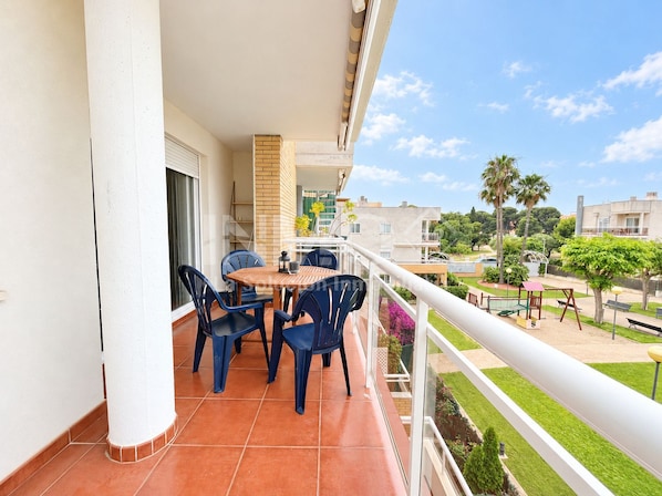 A balcony with a table and chairs, a railing, and a view of a residential area with greenery and buildings.