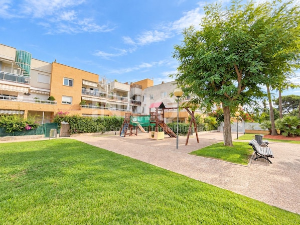 A residential building with a playground, green lawn, and a bench.