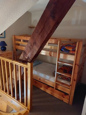 A wooden bunk bed with a slanted ceiling, a nightstand with a lamp, and a small shelf.