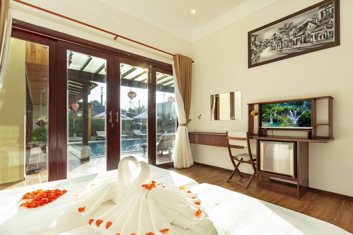 A hotel room with a bed, a television, a desk, and a view of a swimming pool.