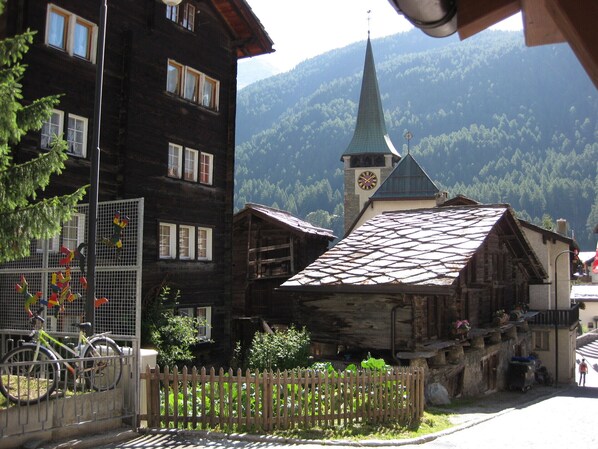 A traditional wooden building with a clock tower, surrounded by a wooden fence and greenery.