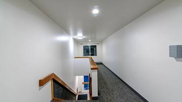 A narrow hallway with a carpeted floor, a wooden staircase, and a window at the end.