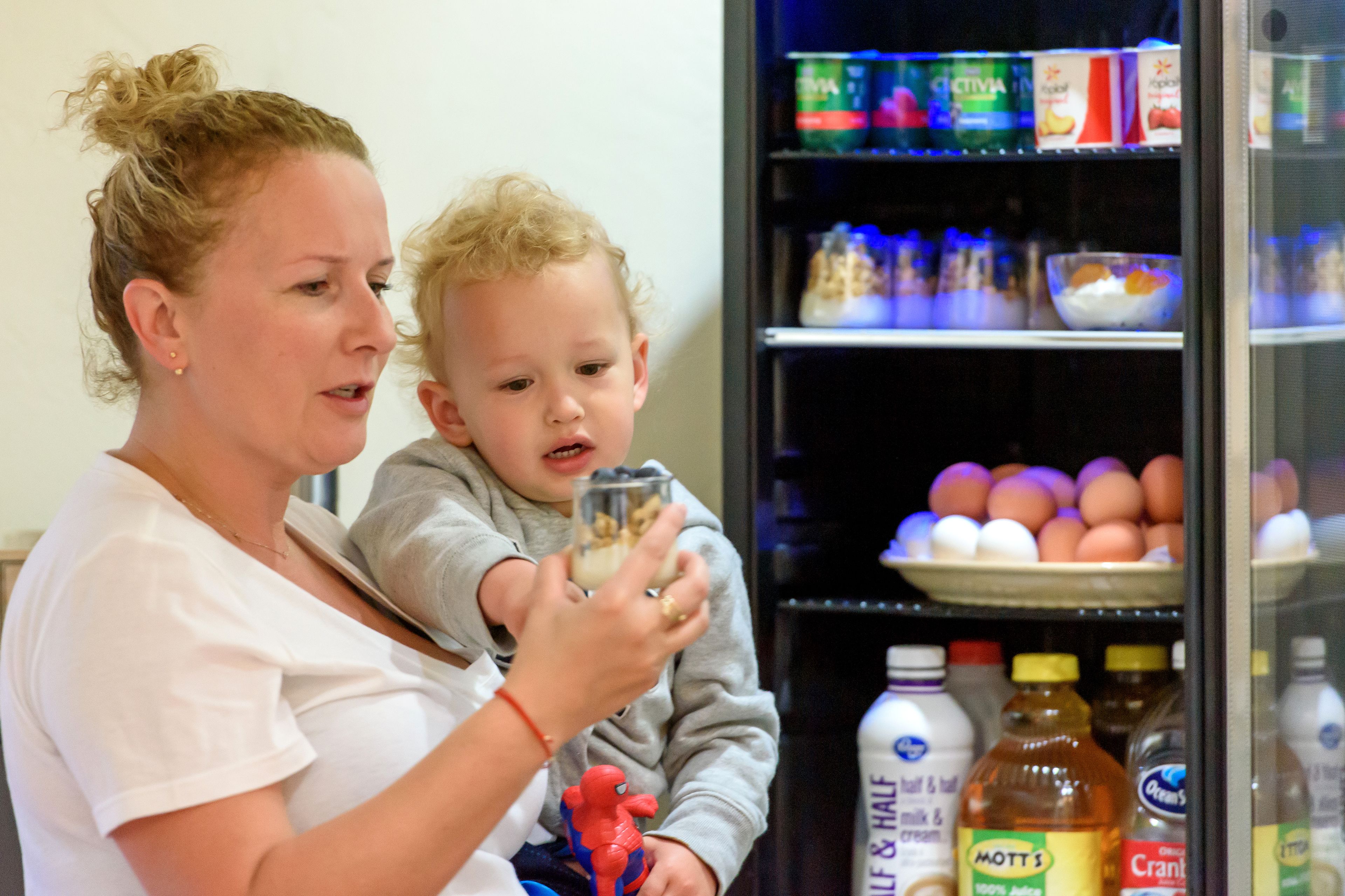 A woman and a child in a room with a refrigerator stocked with various food items.
