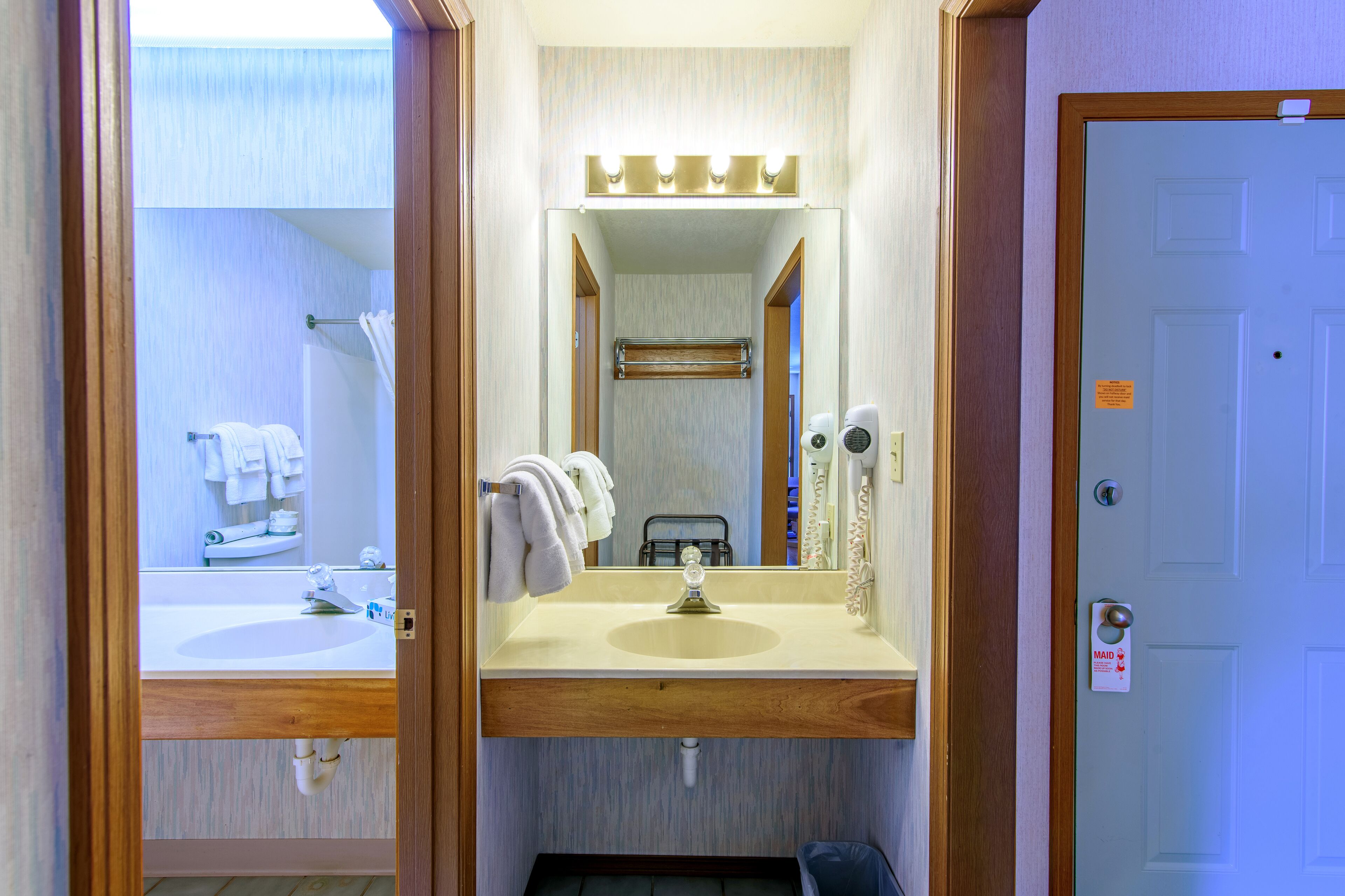 Un baño con lavamanos, espejo, toallero y puerta con el letrero de servicio de limpieza.