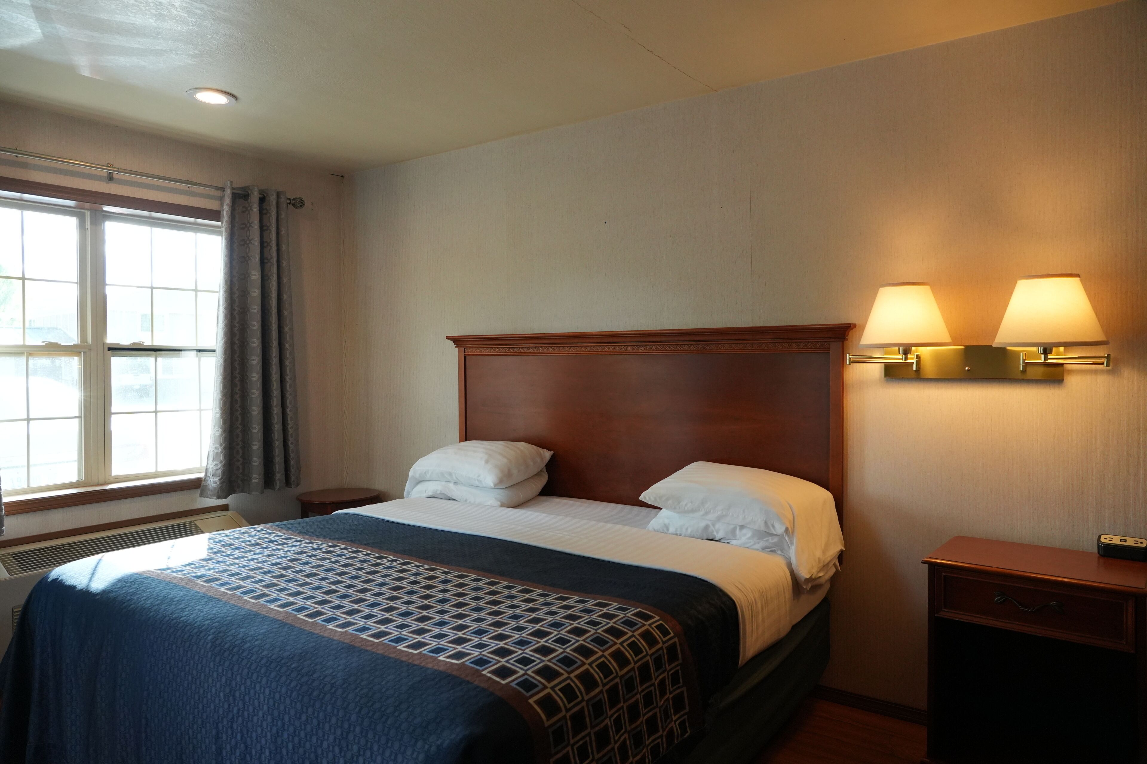 A hotel room with a large bed, two bedside lamps, a nightstand, and a window with curtains.