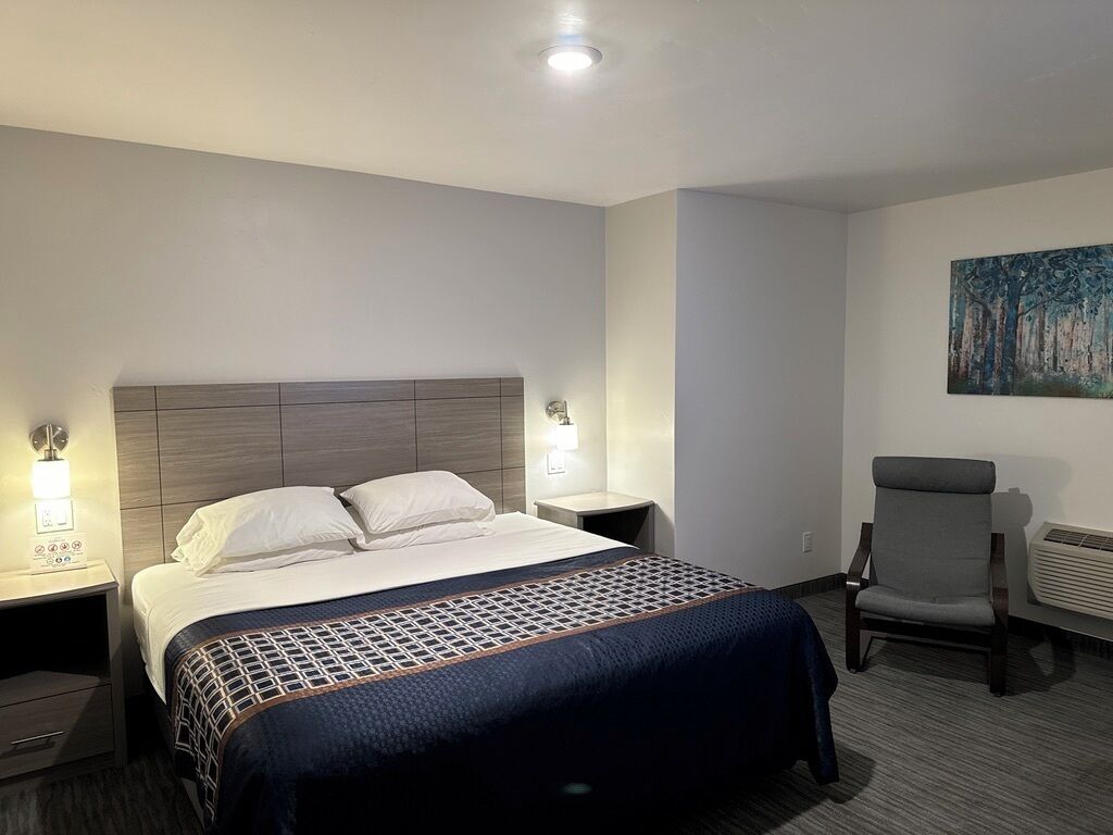 Una habitación de hotel con una cama, lámparas de noche, una silla y un cuadro en la pared.