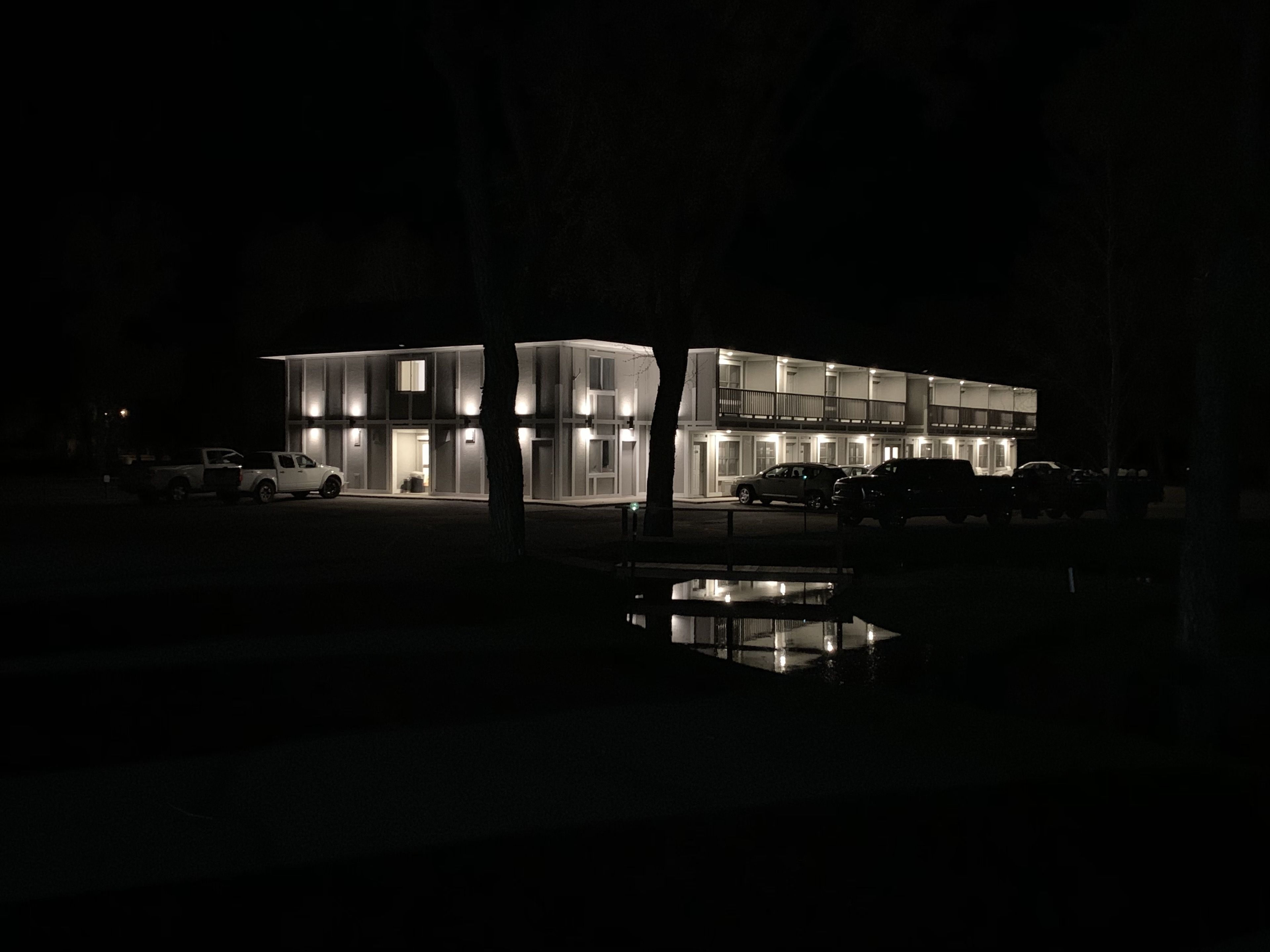 A modern, multi-story building with illuminated windows and a reflective pool in front.