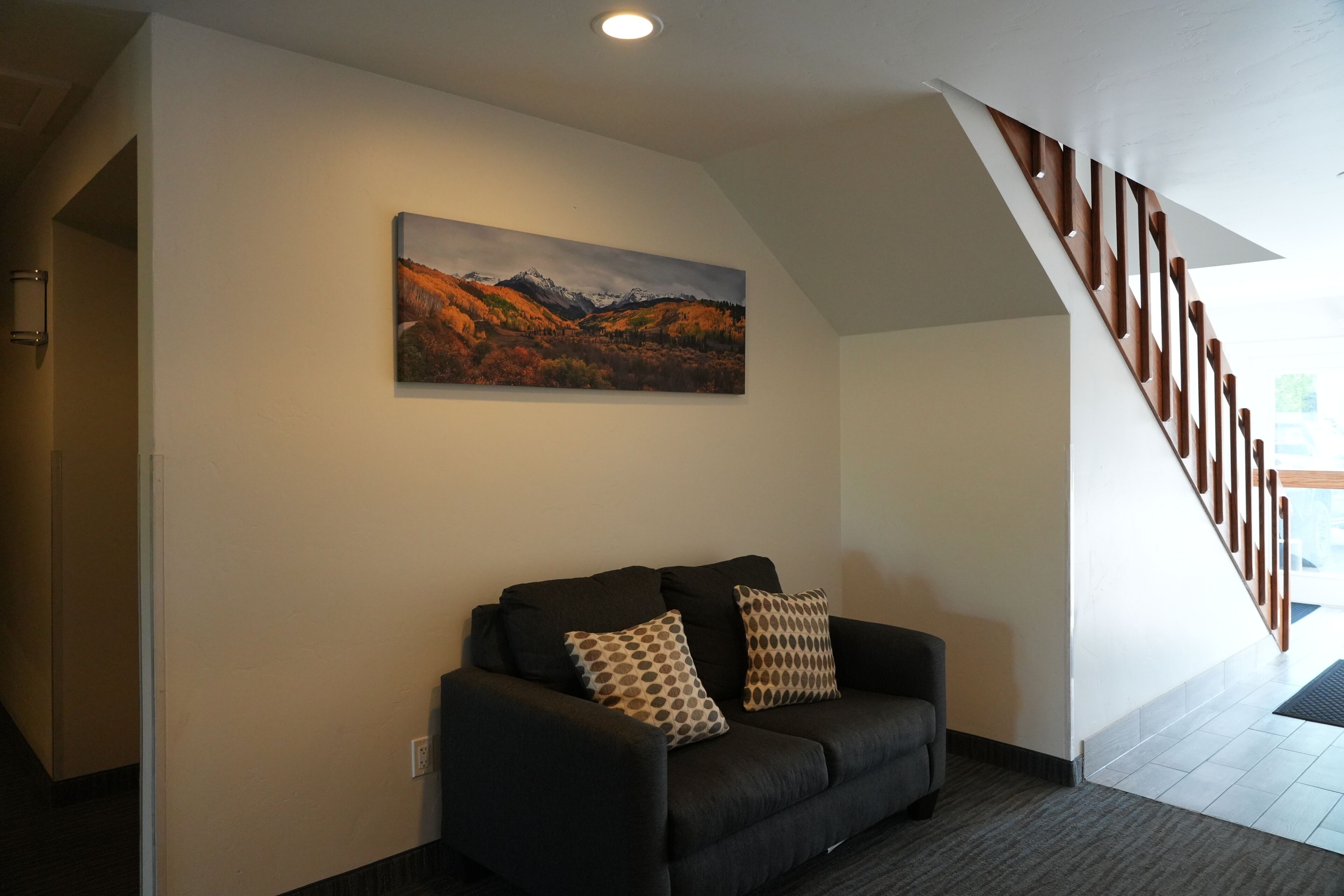 A modern interior with a black sofa, patterned cushions, a landscape painting, and a wooden staircase.