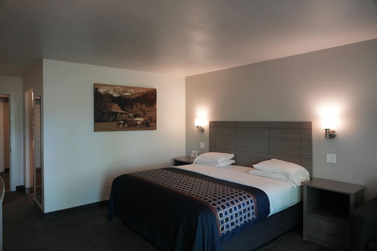 A hotel room with a bed, nightstands, a wall-mounted painting, and two wall-mounted lights.
