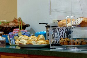 A buffet counter with various baked goods, including bread and muffins, displayed on a glass case. - The Gunnison Inn at Dos Rios Golf Course (Gunnison)