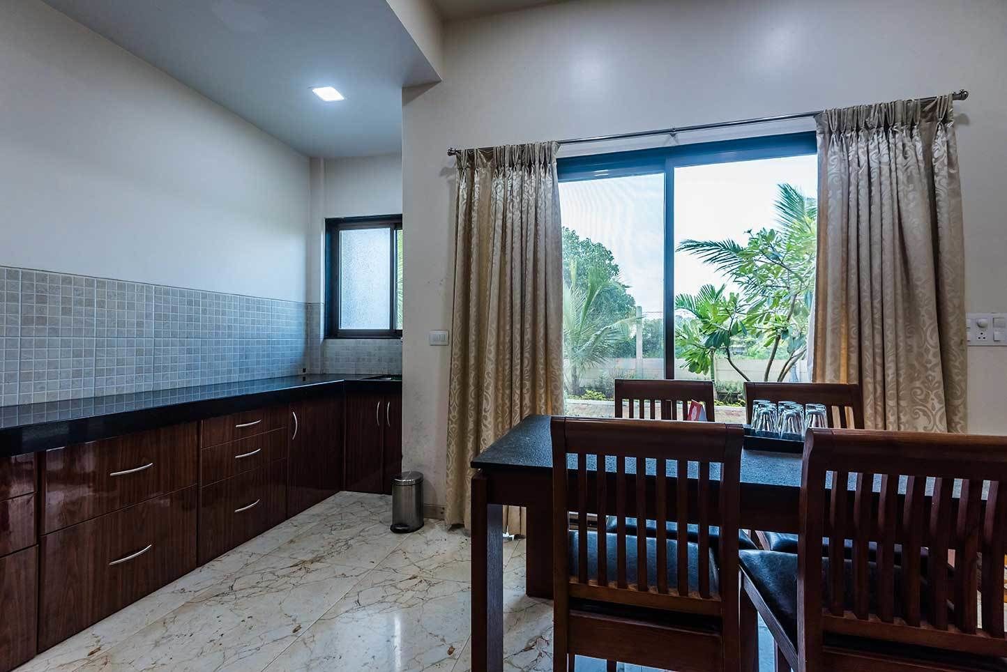 Una cocina con gabinetes de madera oscura, encimera de mármol y comedor con mesa y sillas.