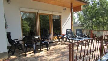 Un patio al aire libre con una mesa y sillas, un espacio de estar cubierto y una barandilla.